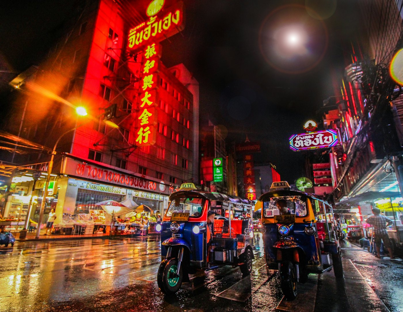 Tuk-tuks under neon signs on a Bangkok street at night