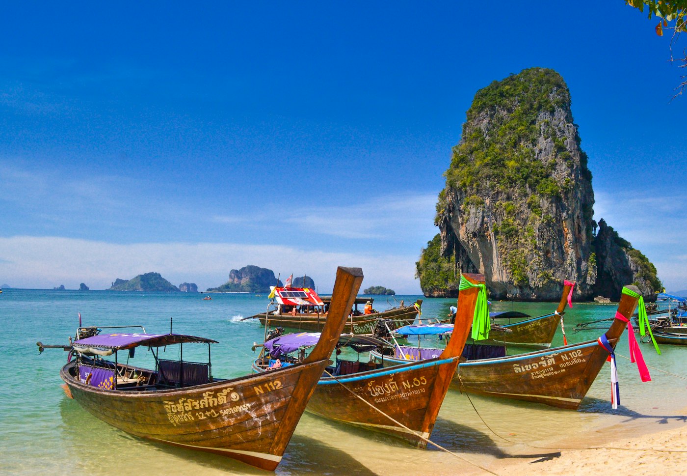 Long-tail boats moored at a beach beside a limestone cliff in Thailand